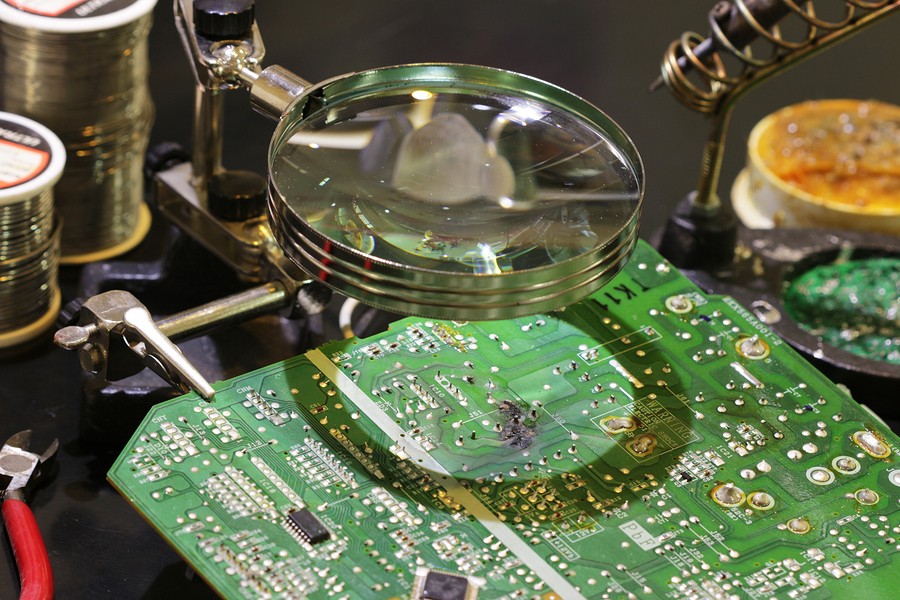 A circuit board being repaired under a magnifying glass