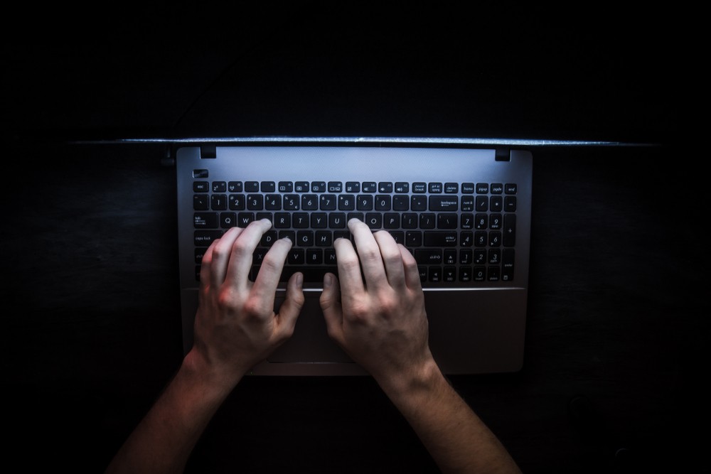 Two hands in a dark room typing on a laptop