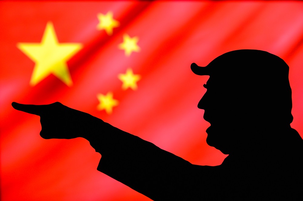 Silhouette of Trump speaking and pointing with China flag behind him