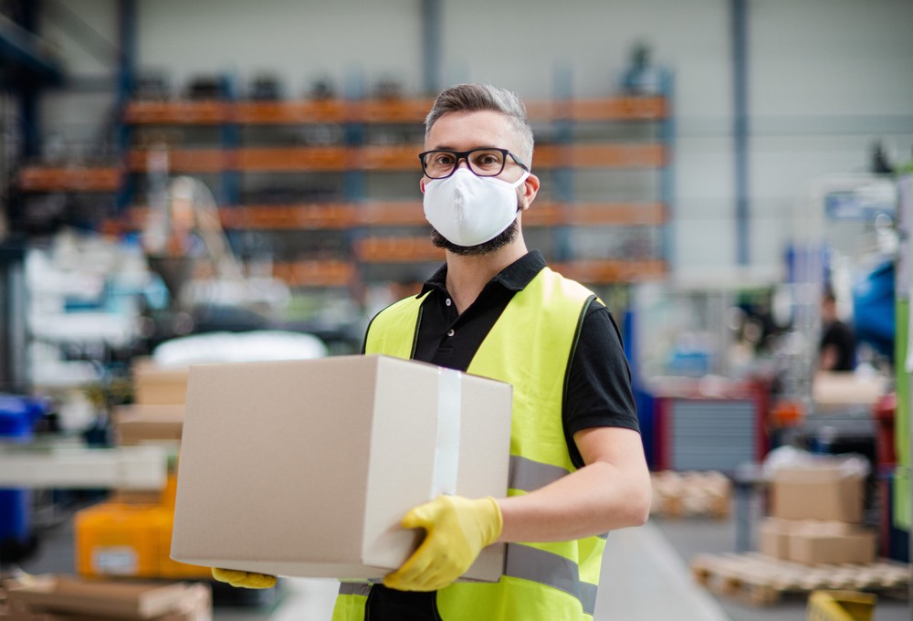 Factory worker with a protective mask and gloves carrying a box