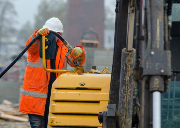 Construction Worker In Safety Gloovs Filling Excavator With Diesel Fuel