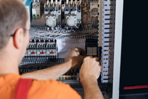 Back View Worker Technician Adjusting Industrial Control Panel In Factory.