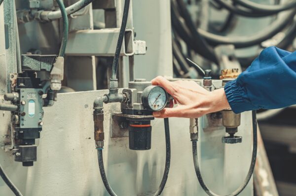 Technician Adjusting Pressure Regulator With Gauge On Industrial Machinery