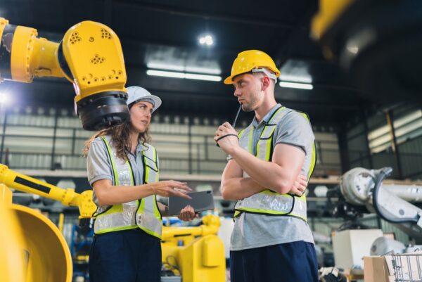 Two Engineers Discussing Robotic Arm Operation In A Modern Factory