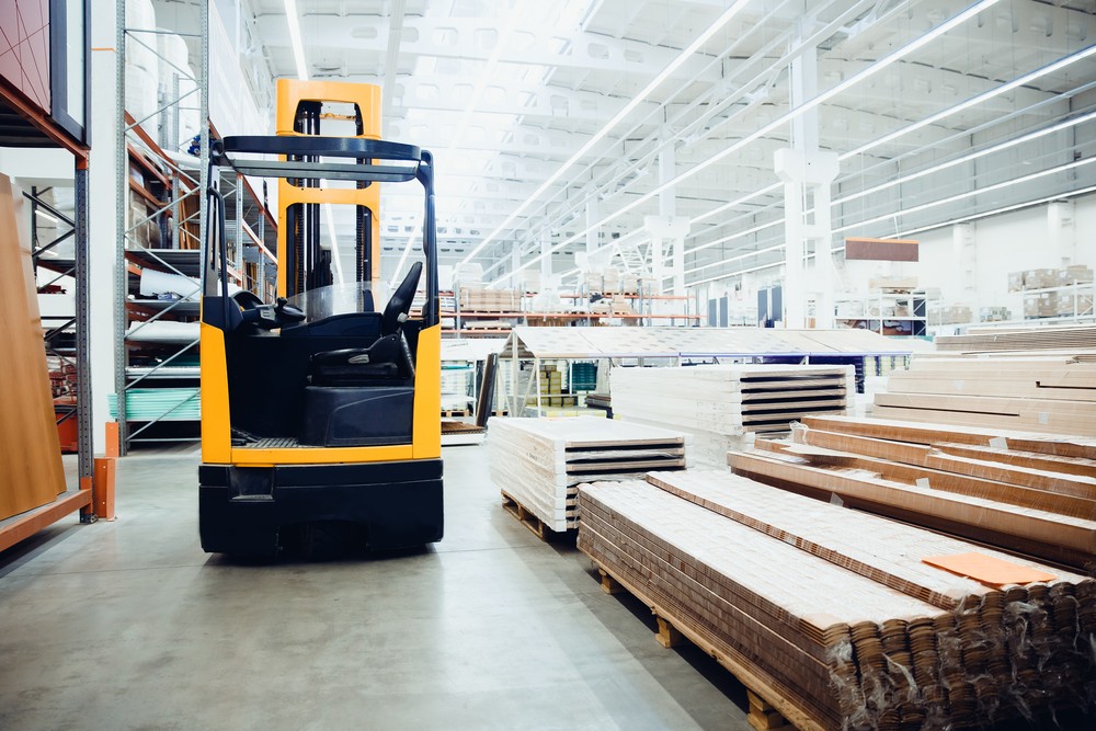 A forklift driving past piles of lumbar in a warehouse