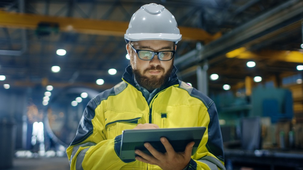 An engineer with a hardhat in a factory looking at an iPad